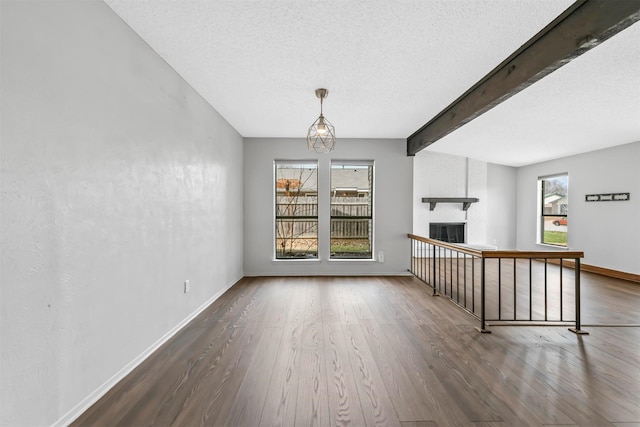 empty room featuring beam ceiling, wood finished floors, a fireplace, and baseboards