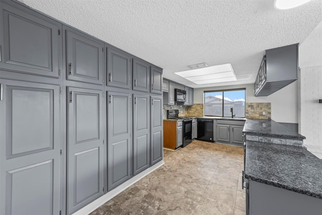 kitchen with backsplash, dark stone countertops, a skylight, black appliances, and a sink