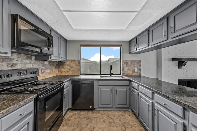 kitchen featuring dark stone counters, gray cabinetry, decorative backsplash, black appliances, and a sink