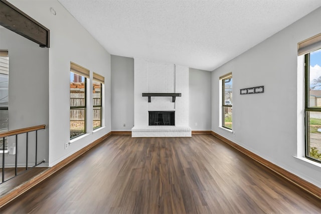 unfurnished living room with dark wood finished floors, a brick fireplace, a wealth of natural light, and a textured ceiling