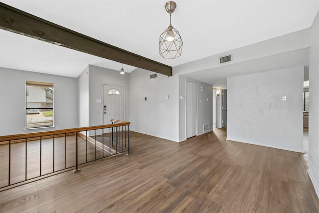 spare room with beam ceiling, wood finished floors, and visible vents