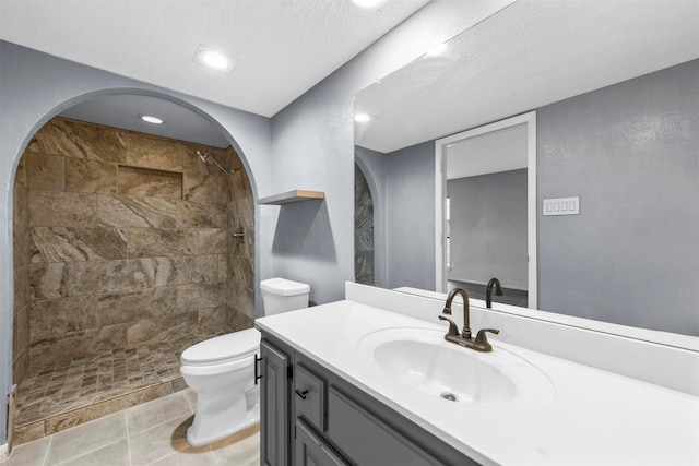 bathroom featuring vanity, a tile shower, a textured ceiling, tile patterned floors, and toilet