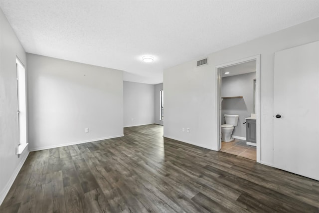 spare room with visible vents, a textured ceiling, baseboards, and dark wood-style flooring