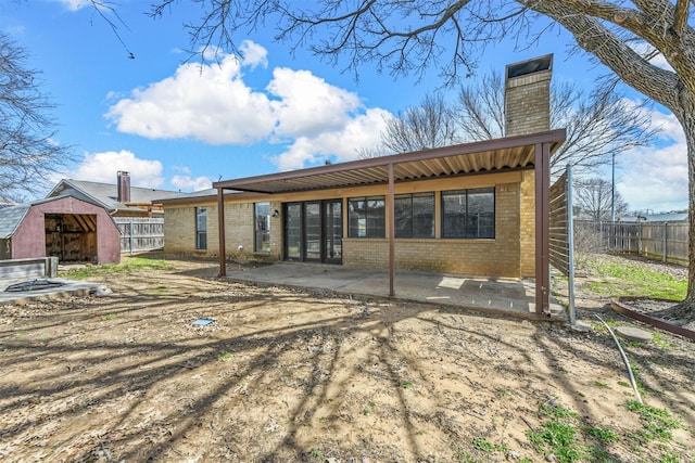 rear view of house featuring brick siding, a chimney, a patio, and fence