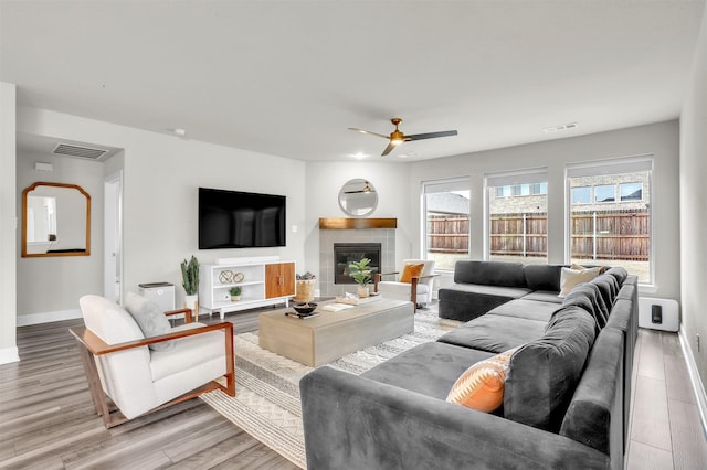 living room featuring a tiled fireplace, light wood-style floors, visible vents, and baseboards