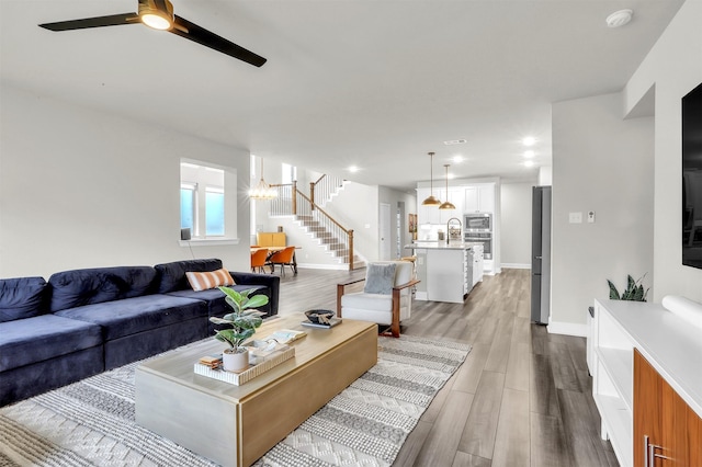 living area with stairs, wood finished floors, baseboards, and a ceiling fan