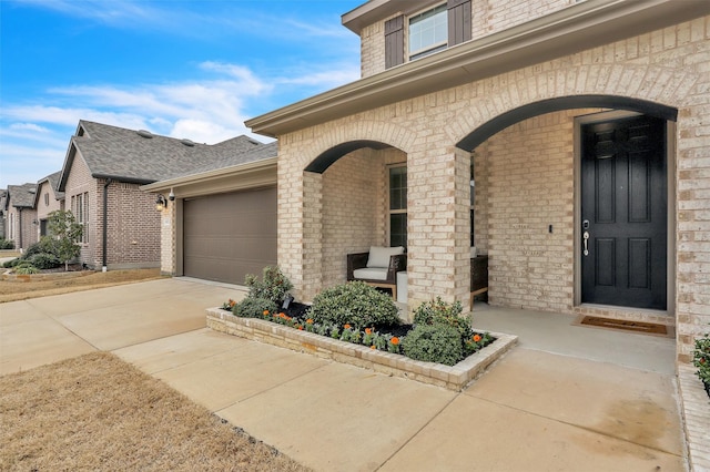 property entrance featuring brick siding, a shingled roof, concrete driveway, covered porch, and a garage