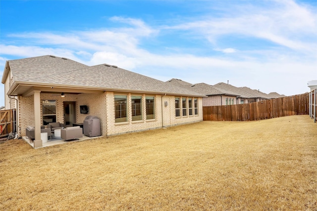 rear view of property featuring a patio, a fenced backyard, a yard, roof with shingles, and brick siding