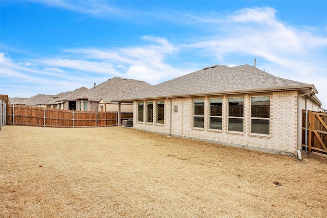 rear view of house with brick siding, roof with shingles, and a fenced backyard