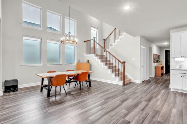 dining space with light wood finished floors, stairway, an inviting chandelier, and baseboards