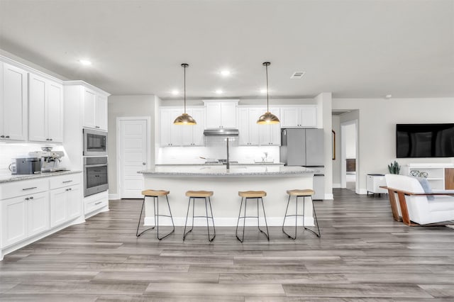 kitchen with a center island with sink, decorative backsplash, under cabinet range hood, appliances with stainless steel finishes, and white cabinetry