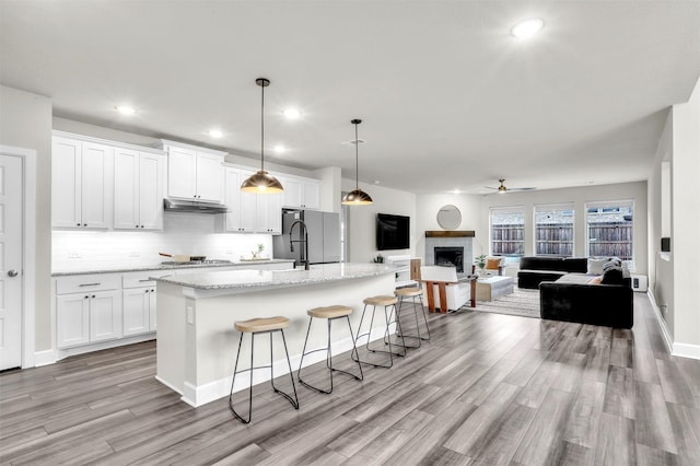 kitchen with under cabinet range hood, open floor plan, white cabinetry, and stainless steel appliances