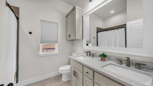 bathroom featuring double vanity, toilet, baseboards, and a sink