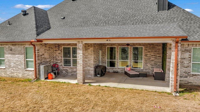 rear view of property with brick siding, a shingled roof, and a patio