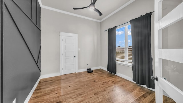 spare room with baseboards, crown molding, a ceiling fan, and wood finished floors