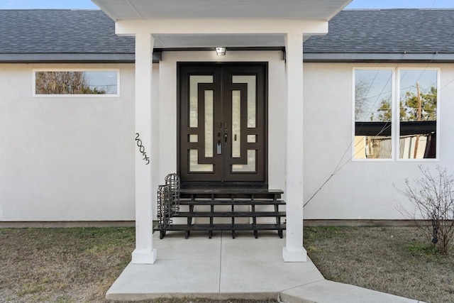 doorway to property featuring stucco siding and roof with shingles