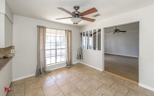 unfurnished dining area with light tile patterned floors, a ceiling fan, visible vents, and wainscoting