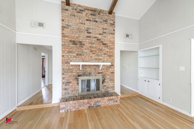 unfurnished living room with visible vents, beamed ceiling, a fireplace, and wood finished floors