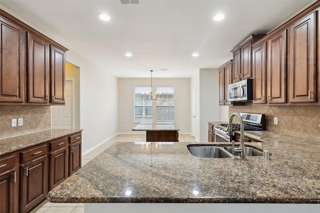 kitchen with a kitchen island, dark stone counters, light tile patterned floors, appliances with stainless steel finishes, and a sink