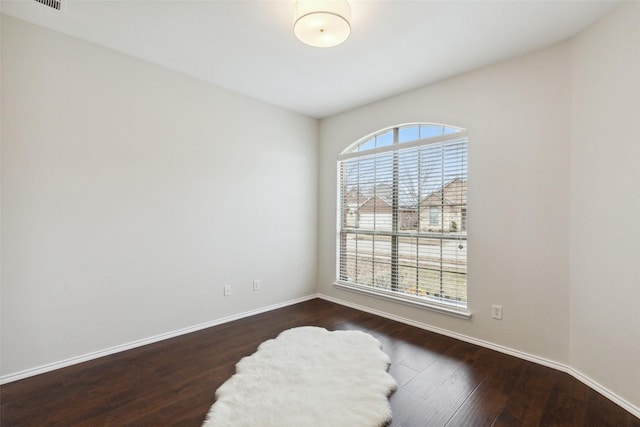 empty room featuring dark wood finished floors, visible vents, and baseboards