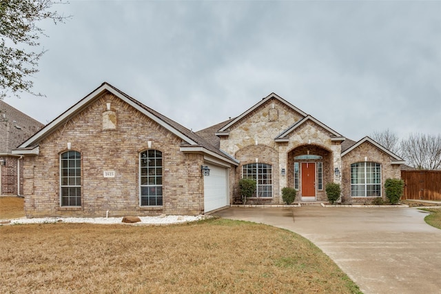 french provincial home with a front yard, fence, an attached garage, concrete driveway, and brick siding