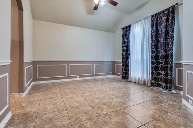 tiled spare room with lofted ceiling, ceiling fan, wainscoting, and a decorative wall