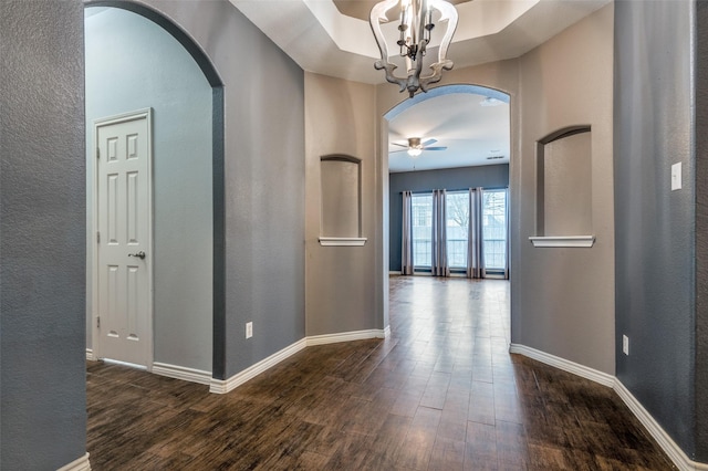 hallway featuring dark wood-style floors, arched walkways, and baseboards