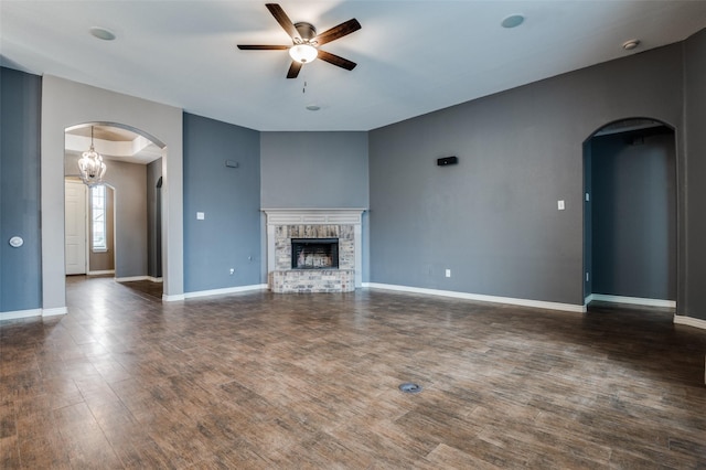 unfurnished living room with wood finished floors, baseboards, a fireplace, arched walkways, and ceiling fan with notable chandelier