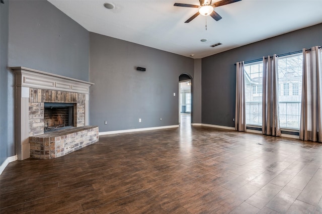 unfurnished living room with wood finished floors, arched walkways, a fireplace, baseboards, and ceiling fan