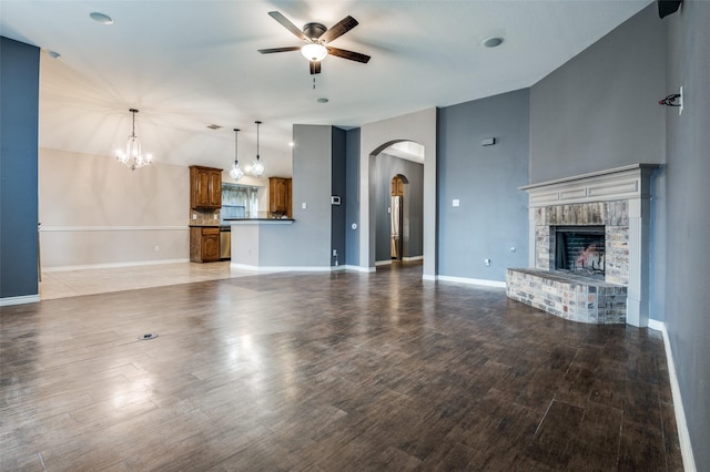 unfurnished living room with wood finished floors, lofted ceiling, arched walkways, ceiling fan, and a brick fireplace