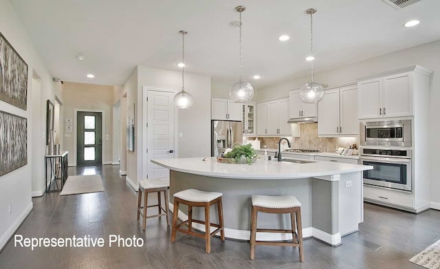 kitchen featuring a kitchen bar, a sink, stainless steel appliances, light countertops, and decorative backsplash