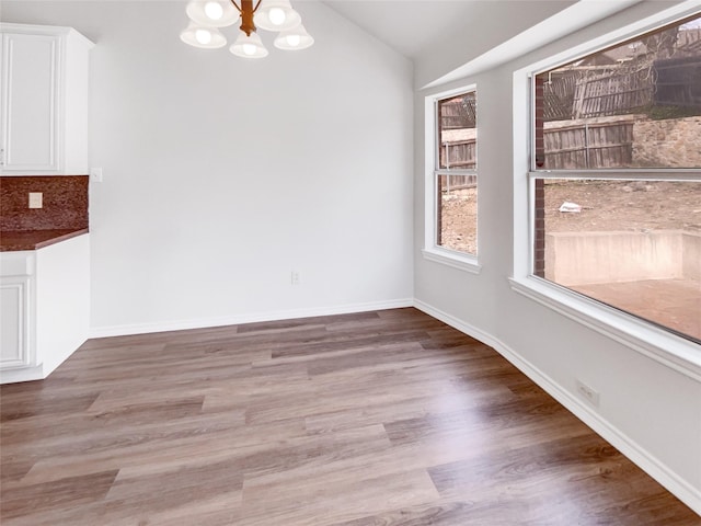 unfurnished dining area with baseboards, lofted ceiling, an inviting chandelier, and wood finished floors