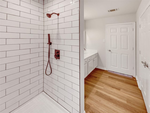 bathroom with visible vents, wood finished floors, a tile shower, baseboards, and vanity