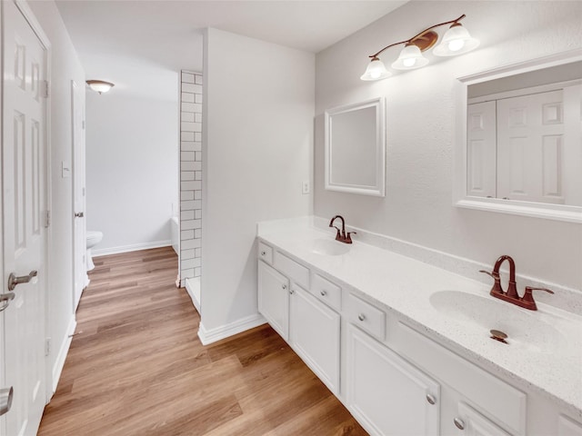 bathroom featuring double vanity, wood finished floors, toilet, and a sink