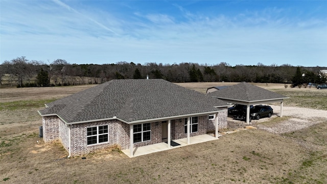 rear view of property with a yard, brick siding, roof with shingles, and a carport