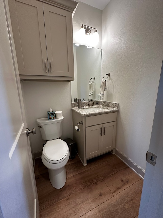 bathroom featuring toilet, vanity, baseboards, and wood finished floors