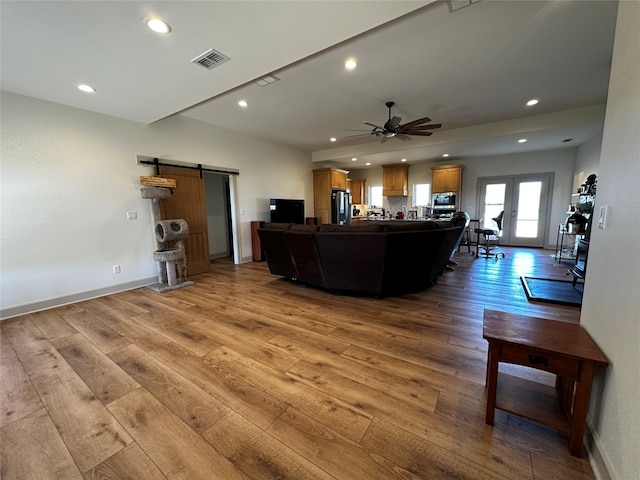 living room with a barn door, recessed lighting, wood finished floors, and visible vents