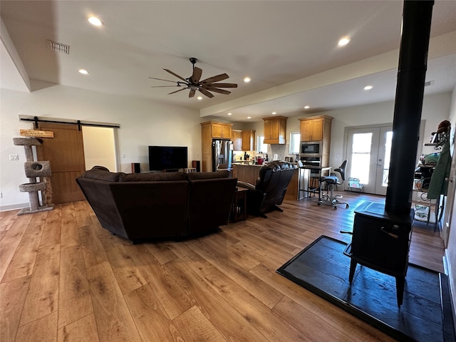 living area featuring visible vents, light wood-style flooring, recessed lighting, ceiling fan, and a barn door