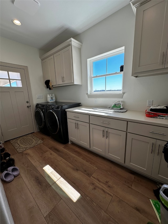 clothes washing area featuring dark wood finished floors, washing machine and dryer, cabinet space, and a healthy amount of sunlight