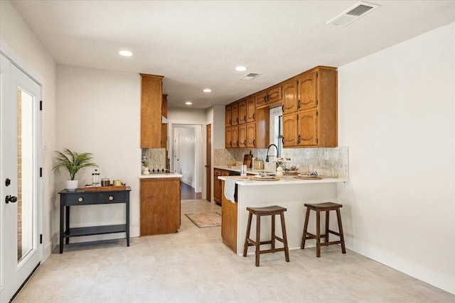 kitchen with a peninsula, decorative backsplash, light countertops, and brown cabinets