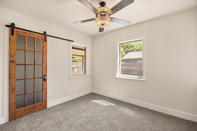 carpeted empty room featuring a barn door, a ceiling fan, and baseboards