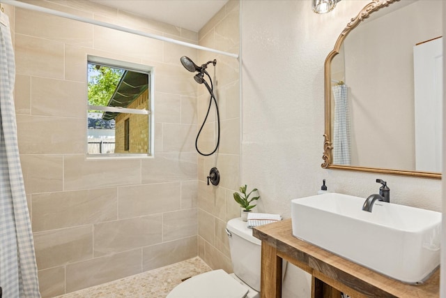 bathroom featuring toilet, tiled shower, and a sink