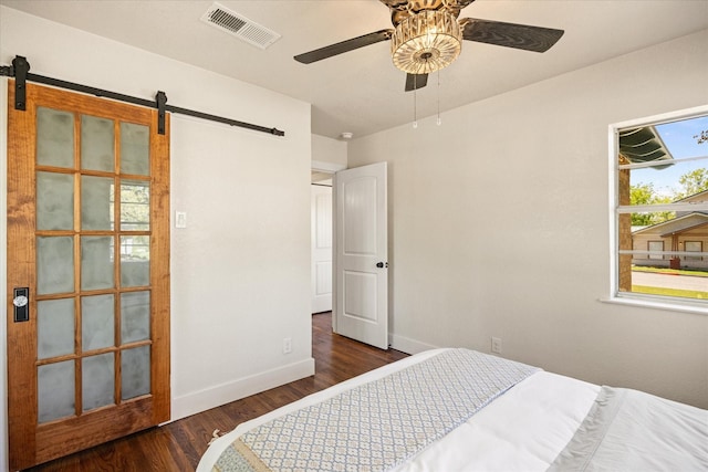 bedroom with wood finished floors, visible vents, a barn door, baseboards, and ceiling fan