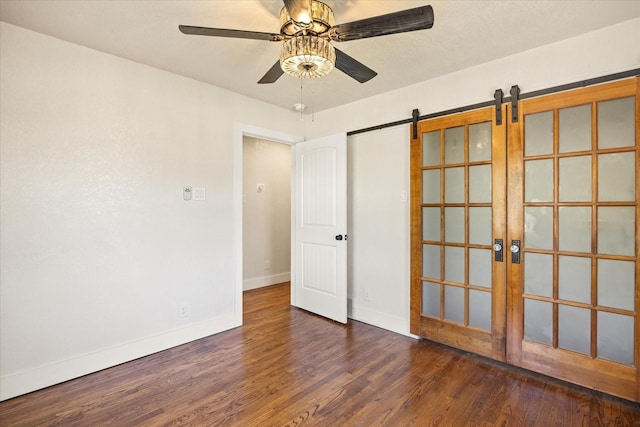 unfurnished room with baseboards, a barn door, ceiling fan, and wood finished floors