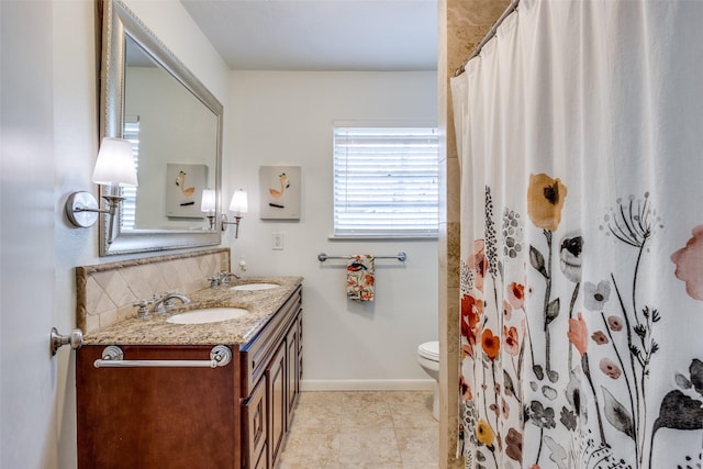 bathroom featuring a sink, baseboards, toilet, and double vanity