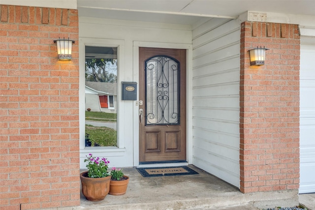 view of exterior entry featuring a garage and brick siding