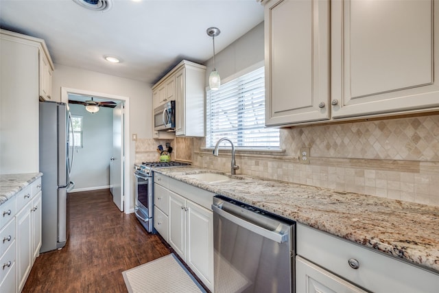 kitchen with light stone countertops, dark wood finished floors, a sink, decorative backsplash, and stainless steel appliances