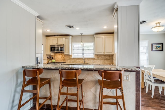 kitchen with a breakfast bar, cream cabinetry, stainless steel microwave, and light stone counters