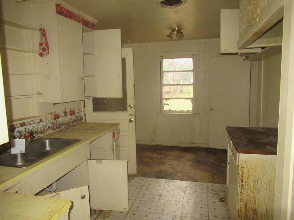 kitchen with visible vents, light floors, white cabinets, and a sink