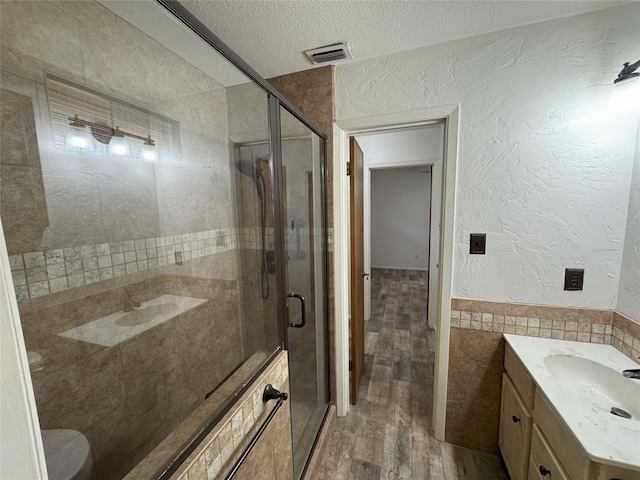 bathroom featuring visible vents, tile walls, a stall shower, a textured wall, and a textured ceiling